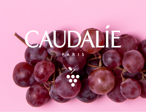Rote Weintrauben auf rosa Hintergrund mit dem Schriftzug 'CAUDALÍE PARIS' und einem stilisierten Traubensymbol
